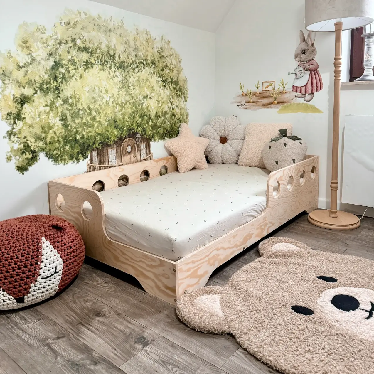 Kinderbett TILA 5 in Naturholz mit Rausfallschutz und runden Ausschnitten, Kinderzimmer mit gemaltem Baum an der Wand und Bären-Teppich.